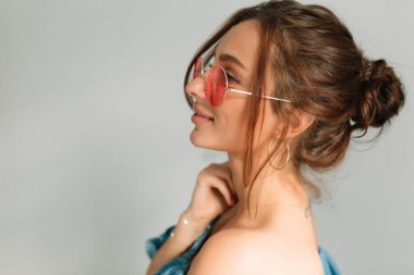 Yuvarlak, zarif, bronz tenli bir kadının profil portresi çenesine dokunuyor ve gün ışığına bakıyor..