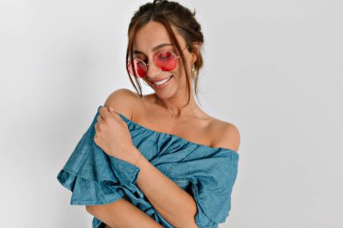 Siyah saçlı, pembe yuvarlak gözlüklü ve çıplak omuzlu kot gömlekli hoş bir bayanın portresi. Yüksek kalite fotoğraf