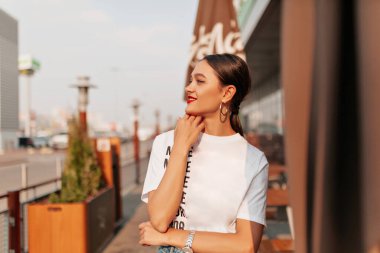 Şehirde beyaz tişörtlü, kırmızı dudaklı çekici Avrupalı bir kızın açık hava portresi. - Evet. Beyaz bluzlu ve kot şortlu, dışarıda eğlenen sevimli genç bir kadının portresi.. 