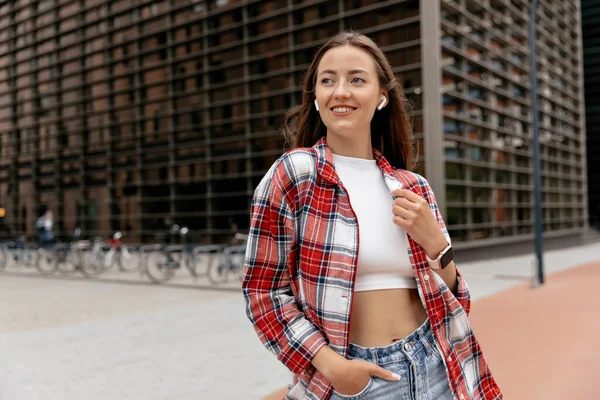 Happy adorable woman with wonderful smile wearing shirt, top and jeans walking on business district in european city on summer morning. European woman spend tine outdoor in warm summer day