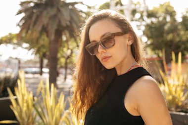 Güneşli yaz akşamlarında bol dalgalı saçlı, günlük kıyafetler giyen zarif ve şık bir kadının profil portresi. Güzel beyaz kız utangaç bir şekilde gülümsüyor.. 