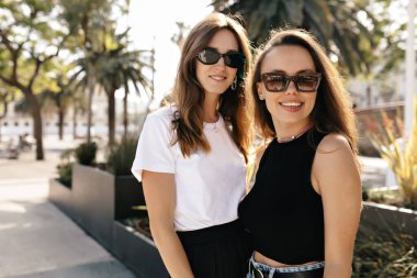 Gülümseyen mutlu beyaz kızlar yaz caddesinde birlikte parkta vakit geçiriyorlar. Gençler güler, yaz günü günlük kıyafetler giyerler. Doğa, tatil konsepti