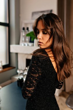 Dalgalı siyah saçlı, arkadan poz veren şık, şık bir kadın. Güzel esmer kadın uzun bir gece elbisesi giyiyor. Kutlama konsepti. 