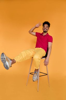 Uzun boylu, esmer, kırmızı tişörtlü ve sarı pantolonlu genç ve çekici bir adamın portresi. 