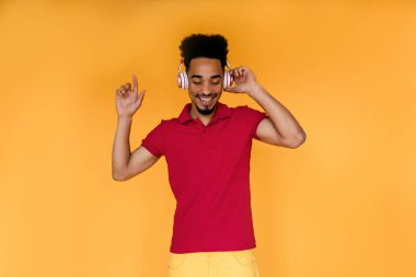 Havalı adam parmağını kaldırır ve sarı arka planda müzik dinler. Kapalı alanda çekilmiş kırmızı tişörtlü bir adamın ıssız bir arka planda dans ederken fotoğrafı.