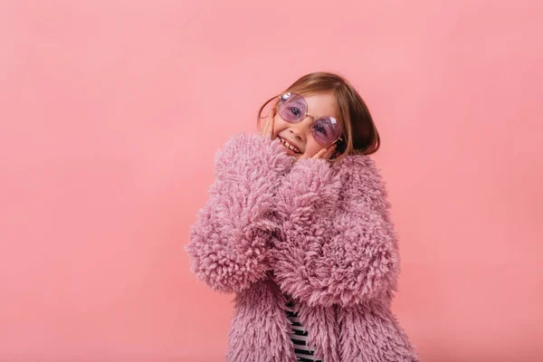 可爱而快乐的小女孩 面带微笑 身穿紫色皮衣 戴着圆圆的眼镜 带着粉红的背景 享受着欢乐 — 图库照片