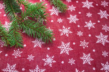 Köknar dalları ve kırmızı zemin üzerinde beyaz kar taneleri olan düz bir çerçeve. Metin için boşluk.