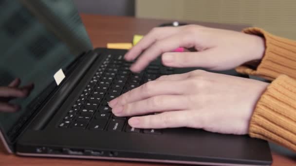 Vista lateral de un freelancers manos escribiendo en el teclado del ordenador portátil y utilizando el teléfono inteligente. La mujer trabaja en un portátil y luego toma el teléfono móvil. Vista de cerca, oficina — Vídeos de Stock