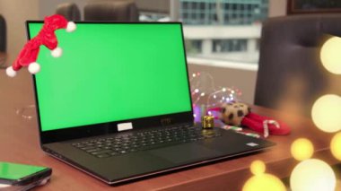 Kapalı kapılar ardında boş yeşil ekran ve Noel süslemesi olan hediye kutusunu dizüstü bilgisayarın klavyesine koyuyor. Tatil konsepti. Ofis. Model