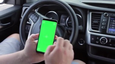 Modern arabalarda boş yeşil ekranlı kromakey cep telefonu kullanan bir adam. Model dokunmatik ekran. Akıllı telefon görüntüsü kaydırılıyor.