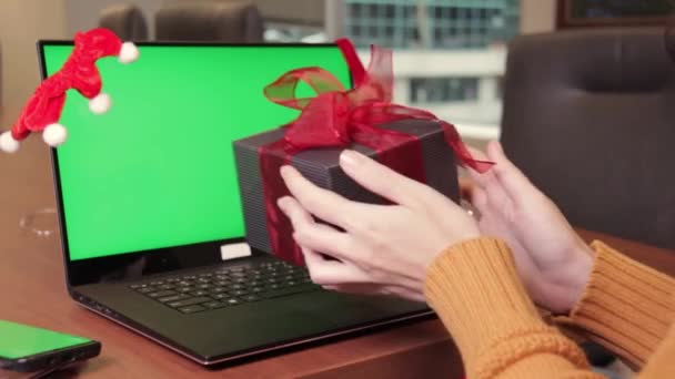 Closeup female hands holding present box using laptop keyboard with empty green screen and Christmas decoration on background. Holiday concept. Video call. Mock-up — Stock Video