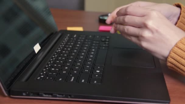 Vista lateral de un freelancers manos escribiendo en el teclado del ordenador portátil y utilizando una nota adhesiva. La mujer trabaja en una computadora portátil y luego escribe en una pegatina. Vista de cerca, oficina — Vídeos de Stock