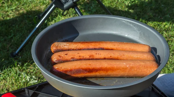 Salsicce di hot dog fritte su un fornello a gas. Salsicce crude su una padella da campeggio. Le salsicce sono fritte sul picnic esterno — Foto Stock