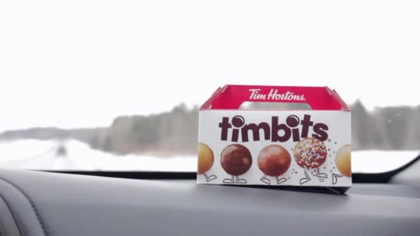 Una caja tamaño snack de Tim Hortons Timbit agujeros de rosquilla en el panel móvil del coche. Viajando con bocadillos canadienses. Montreal, Quebec, Canadá, 11 de enero de 2022 — Vídeos de Stock