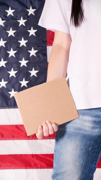Young woman holding blank sign in her hands close up. American flag on background