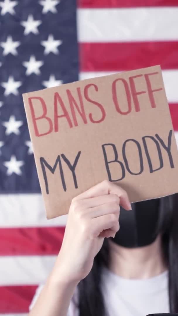 看板を持っている女性は背景に私の体アメリカの旗を禁止します 中絶法の厳格化に対する抗議 全国の女性がストライキを行う Covid 19にフェイスマスクを着用 垂直ビデオ — ストック動画