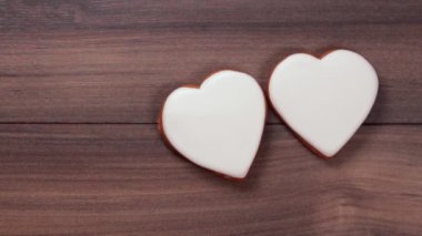 Ahşap arka planda iki büyük kalp kurabiyesi ve onu kurtarmak için kalplerden birini yumuşak bir şekilde alan bir kadın eli. Aşk konsepti. Kırık kalp. Güven yok. Metin için boşluk
