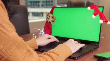 Yeşil, boş, boş bilgisayarlı dizüstü bilgisayar Mutlu Noeller masasında hediyelerle, Noel Baba evinin arka planında süslenmiş Noel ağacıyla sahneleniyor. İnternet sitesi çevrimiçi alışveriş.