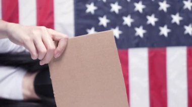 Boş karton pankart gösteren tanınmayan bir kadın. Karton bir kutunun boş posterini tutan eller. Sloganınız, logonuz ya da reklamınız için yer açın. Banner tasarım konsepti. Arka planda Amerikan bayrağı.