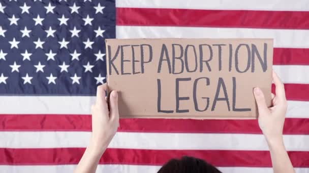 妇女从背后拿着一个标志保持堕胎合法的美国国旗为背景 抗议反堕胎法 女人的罢工 妇女的权利自由 — 图库视频影像