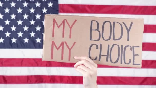背中の女性は私の体私の選択アメリカの旗を背景に署名を保持します 反中絶法に対する抗議 女性のストライキ 女性の権利の自由 — ストック動画
