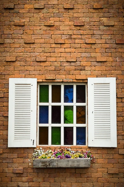 Открытое окно с корзиной цветов на кирпичной стене — стоковое фото