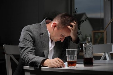 Adam işten sonra mutfakta alkol içiyor. Genç adam şiddetli baş ağrısı ya da migrenden muzdarip mutfakta bir bardak viskiyle oturuyor. alkol bağımlılığı