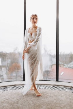 Gelinin sabahı. Mutlu, güzel bir kadın pencerede uzun bir duvak, bornoz ve iç çamaşırı giyiyor. Düğün günü. Doğal güzellik ve profesyonel makyaj. Doğal ışık