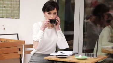 İş kadını cep telefonuyla konuşuyor ve kahve içiyor. Belgelerle çalışan ve dışarıdaki bir kafede akıllı telefondan iletişim kuran bir kadının yan görüntüsü. İş konsepti. İş Şehri Hayatı