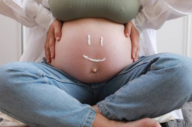 Genç hamile modeli uygulanan nemlendirici streç işaretleri önlemek için karnı üzerinde gövde close-up. Gelecekte anne karnı üzerinde krem nemlendirici gelen komik gülümseme ile. Gebelik cilt bakım kavramı.