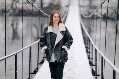 Bir kadın kış günü asma köprüde nehrin üzerinde yürüyor. Soğuk karlı bir günde, kalın elbiseli genç bir kız tahta bir yaya köprüsünde duruyor..