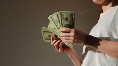 Başarılı bir kadın nakit parayı kontrol ediyor. 100 dolarlık banknotları tutan iş kadını ellerini kapat. Tanınmayan bir kadın elinde dolarlarla eğleniyor. Para ödeme kavramı