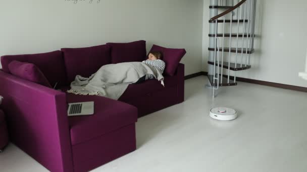 Δωρεάν από τις δουλειές του σπιτιού γυναίκα χαλαρώνει στον καναπέ, ενώ ρομπότ ηλεκτρική σκούπα καθαρισμού. Έννοια της υγιεινής, οικιακά gadgets και ρομπότ στη σύγχρονη ζωή — Αρχείο Βίντεο