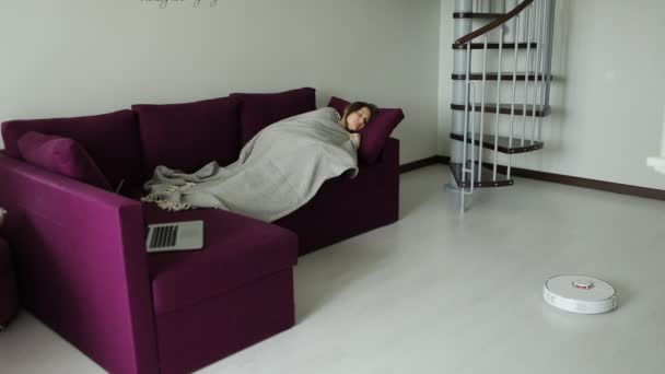Δωρεάν από τις δουλειές του σπιτιού γυναίκα χαλαρώνει στον καναπέ, ενώ ρομπότ ηλεκτρική σκούπα καθαρισμού. Έννοια της υγιεινής, οικιακά gadgets και ρομπότ στη σύγχρονη ζωή — Αρχείο Βίντεο