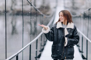 Bir kadın kışın asma köprüsünde yürüyüp nehirde kar taneleri yakalıyor. Soğuk karlı bir günde, kalın elbiseli genç bir kız tahta bir yaya köprüsünde duruyor..