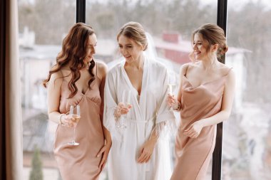 Gelinin sabahı. En iyi nedimelere sahip muhteşem gelin büyük pencerenin yanındaki otel odasında şampanya içiyor. Heyecan verici gecelikli seksi nedimeler. Düğün sabahı detayları.