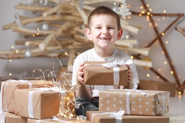 Tatil kavramı. Neşeli küçük çocuk bir hediye kutusu tutuyor. Noel ağacı, bir sürü hediye kutusu ve arka planda süslemeler. Noel, Yeni Yıl, Çocukluk ve İnsanlar Konsepti