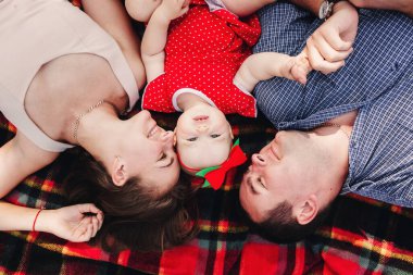 Aile piknikte. Anne, baba ve küçük kız parkta bir battaniyenin üzerinde yatıyorlar. Yaz tatili kavramı. Anneler günü, babalar günü, bebekler günü. Birlikte vakit geçirmek.