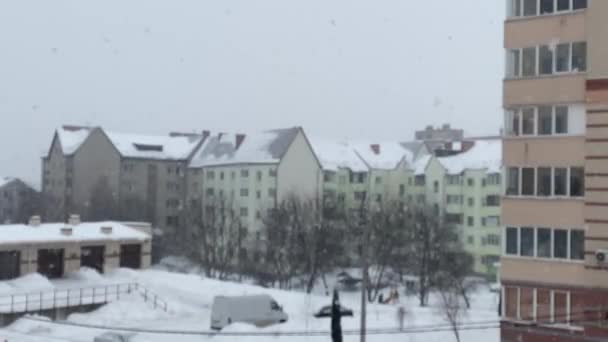Χιονίζει. θολή φόντο της πτώσης μεγάλες νιφάδες χιονιού στο φόντο των κτιρίων κατοικιών. Πέφτει πολύ χιόνι. θέα από το διαμέρισμα — Αρχείο Βίντεο