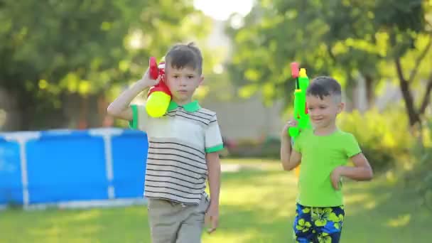 2人の男の子が大きな水鉄砲でカメラに向かっています。夏の晴れた日に子供たちは屋外で楽しんでいます。幸せな子供時代 — ストック動画