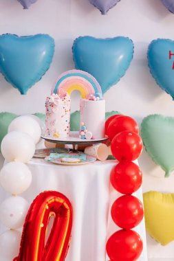 Gökkuşaklı büyük doğum günü pastası, renkli serpintiler. Bir çok renkli kalp balonunun arka planında. Doğum günü partisi. Güzel tatil.
