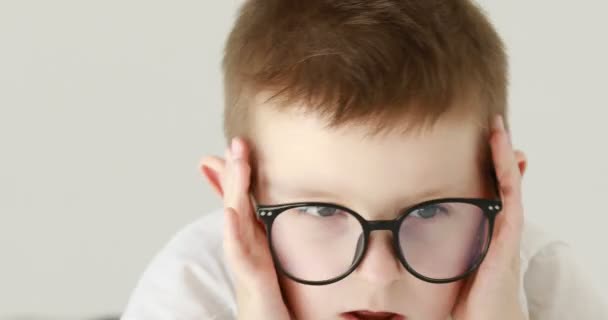 A little boy has a headache, holds his head with his hands. Portrait of caucasian 7 years old boy in glasses. feelings and emotions concept. 4k — 图库视频影像