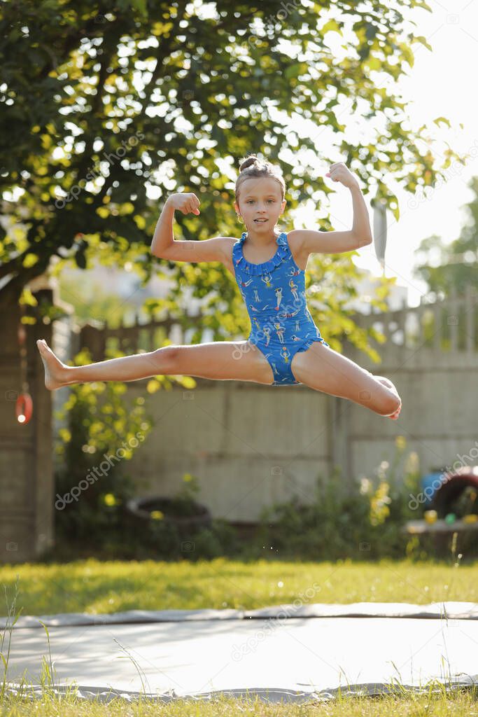 little sports girl jumps on a trampoline. Outdoor shot of girl jumping on trampoline, enjoys jumping in home. happy summer vacation.