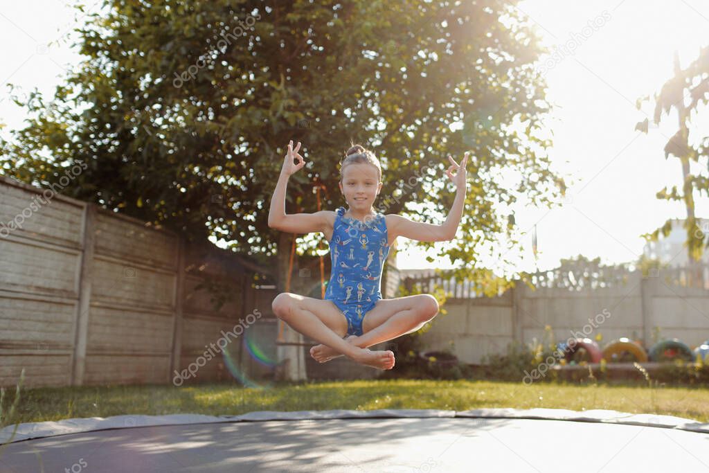 little sports girl jumps on a trampoline. Outdoor shot of girl jumping on trampoline, enjoys jumping in home. happy summer vacation.