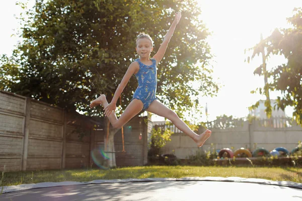 Klein sportmeisje springt op een trampoline. Outdoor shot van meisje springen op trampoline, geniet springen in huis. Fijne zomervakantie — Stockfoto