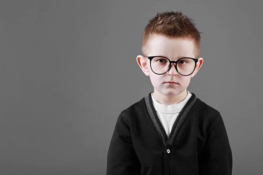 Gri arka planda gözlüklü, zeki ve üzgün bir çocuğun portresi. Okul eğitimi, bilim ve yenilik kavramı, iş geliştirme. Boşluğu kopyala.