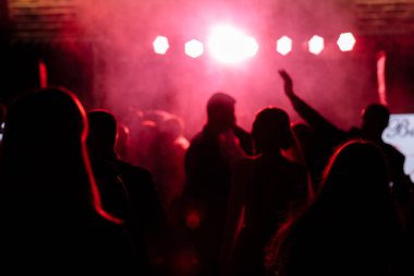 Parlak kırmızı sahne ışıkları önünde tezahürat yapan kalabalık. Disko gece kulübünde dans eden ya da müzik festivalinde konser veren insanların silüeti.