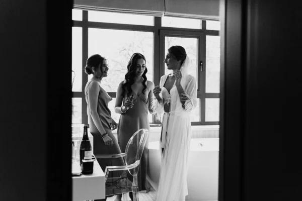白黒写真です 花嫁の朝 最高の新婦付添人と豪華な花嫁は大きな窓の近くのホテルの部屋で楽しんでいます 興奮した怠惰のセクシーな新婦付添人 結婚式の朝の詳細 — ストック写真