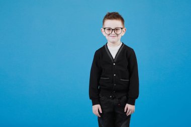 Gözlüklü küçük sevimli çocuk gülümsüyor ve gri arka planda yalnız başına eğleniyor. Mutlu çocukluk. Boşluğu kopyala.