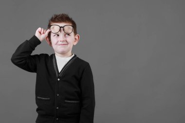 Akıllı çocuk gözlüklerini ayarlar ve gri arka planda eğlenir, yakın plan. Günlük kıyafetlerle çocuk portresi. Boşluğu kopyala.